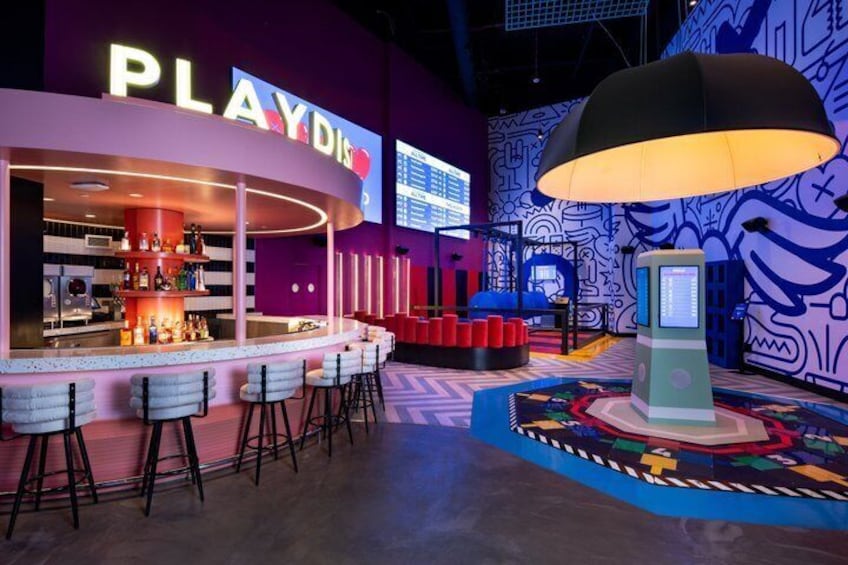 A PlayDPI bar with stools, a large umbrella, and a colorful patterned floor. 3