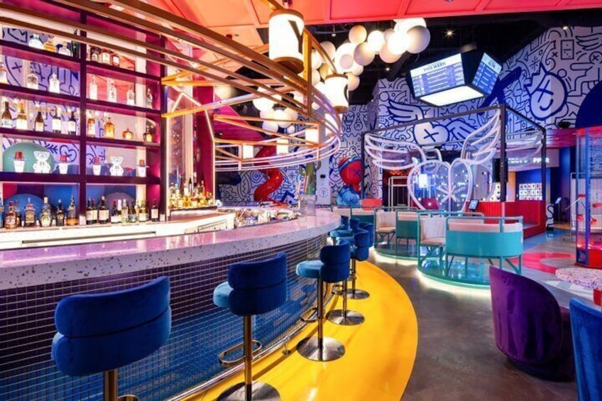 A vibrant bar with colorful decor, blue bar stools, and a variety of bottles on shelves. 4