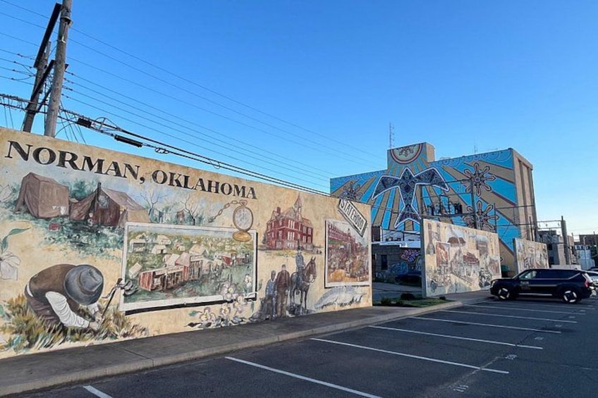 A mural on a building in Norman, Oklahoma, depicting historical scenes and a large clock tower. 4