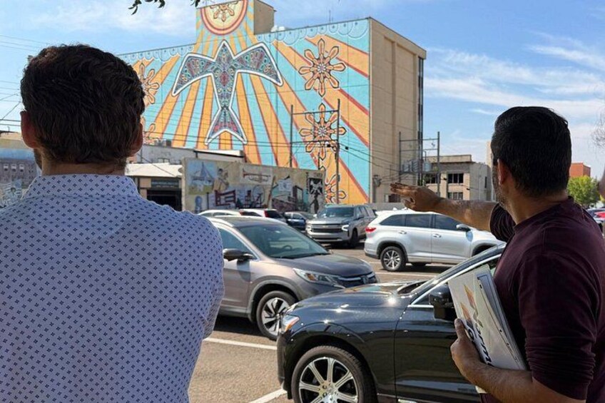Two men observing a colorful mural on a building. 3