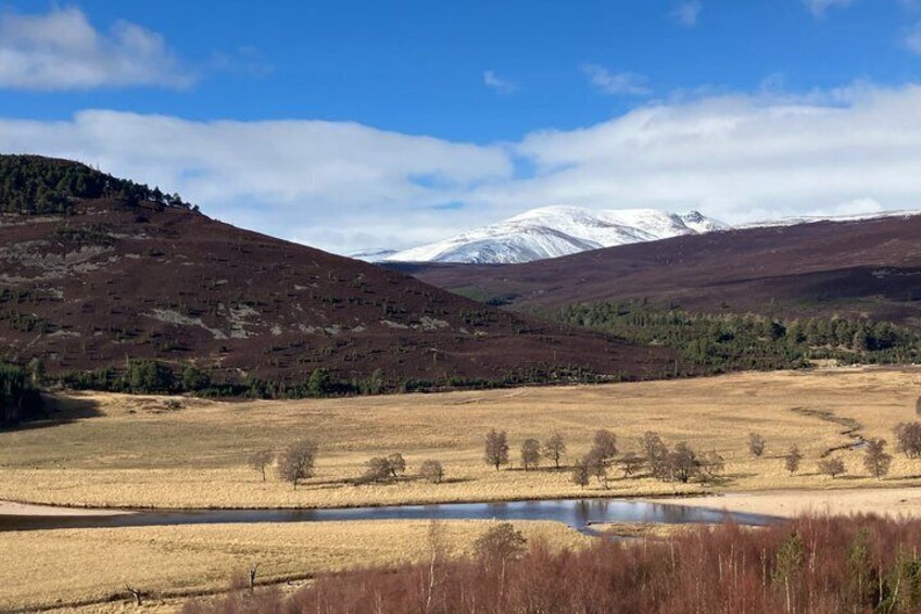 A hilly landscape with a lake, a snow-capped mountain in the background, and a clear blue sky. 4