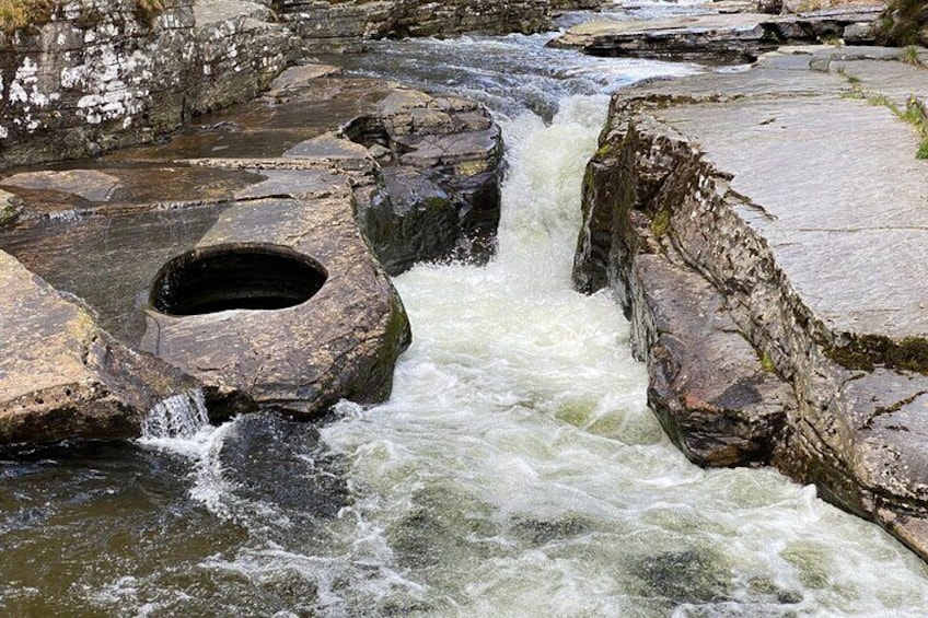 A rocky riverbed with a waterfall and a circular opening. 1