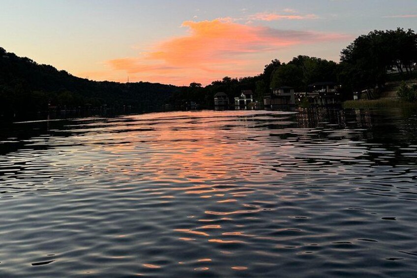 A calm river at sunset with reflections of the sky, surrounded by hills and houses. 2