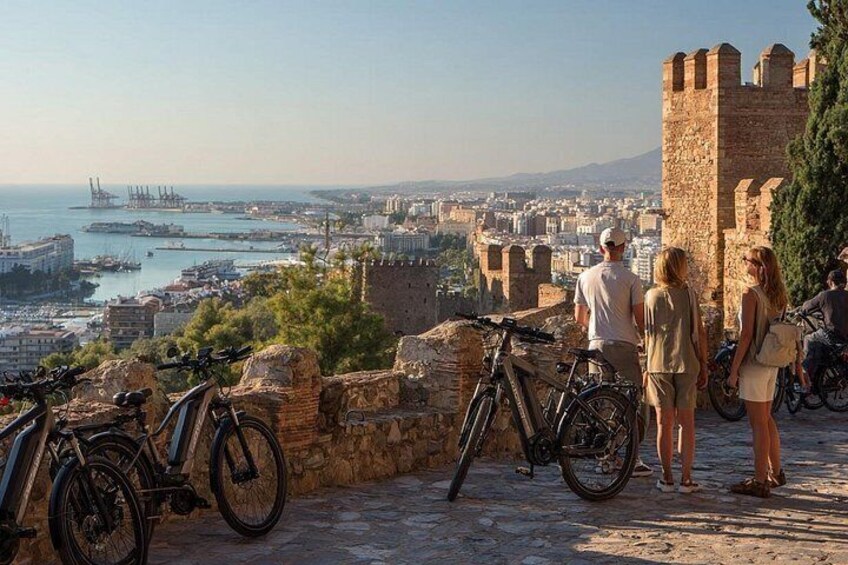 Un paisaje urbano costero con una fortaleza histórica, bicicletas y vistas al puerto. 5