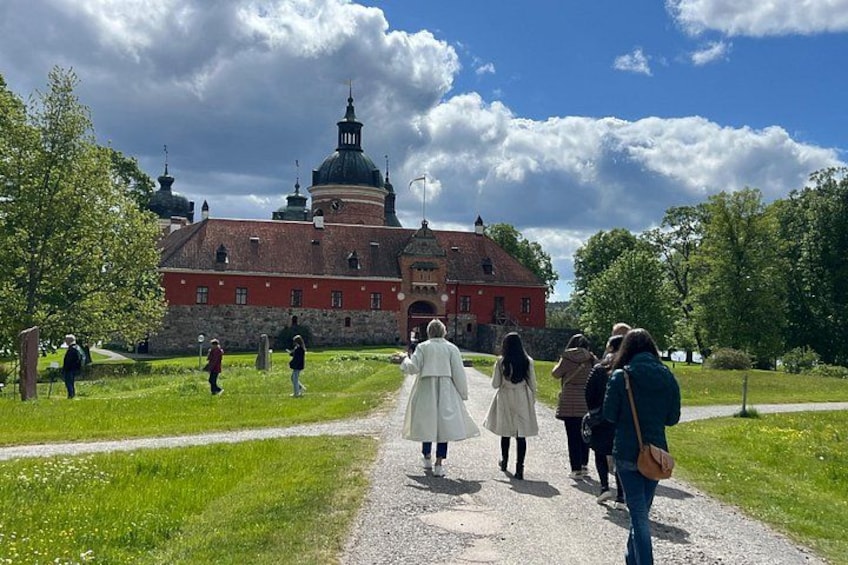 En gruppe mennesker går på en grussti mod en stor, rød bygning med kuppelformede tage. 1