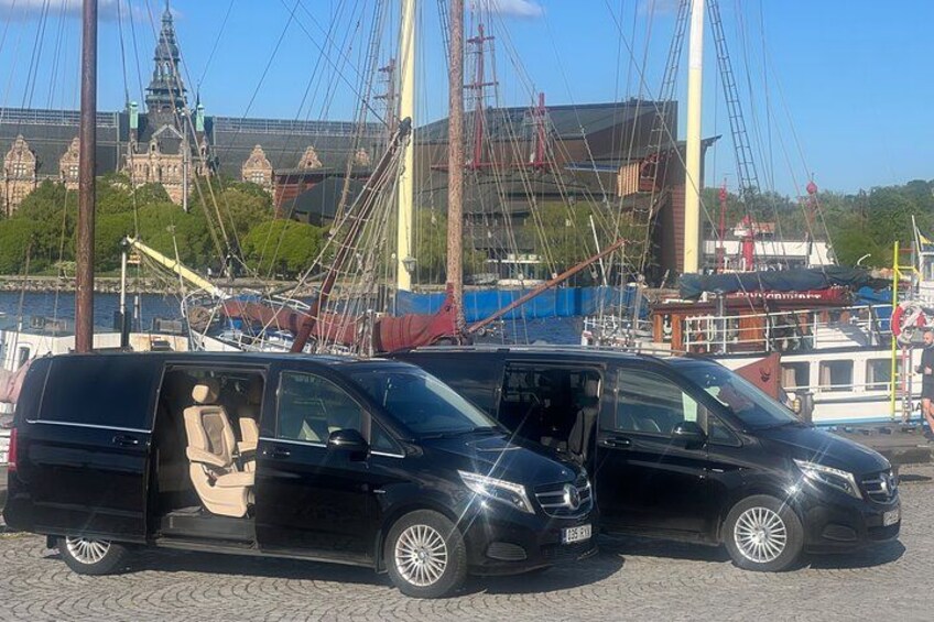 To sorte varevogne parkeret på brosten i nærheden af en kaj med både og en historisk bygning i baggrunden. 2