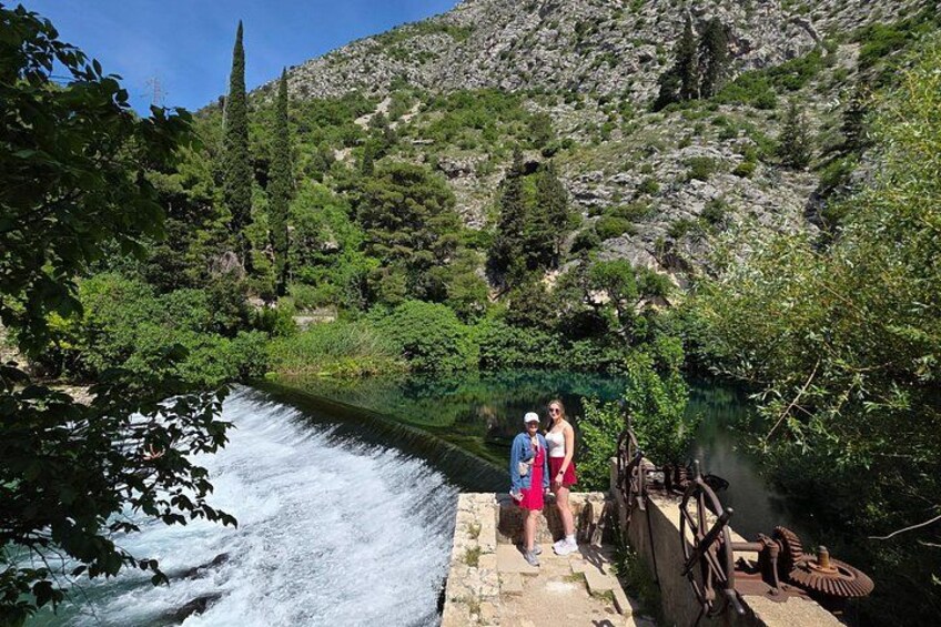 Een rivier met een waterval, een rotsachtige helling en twee personen die op een stenen brug staan. 1