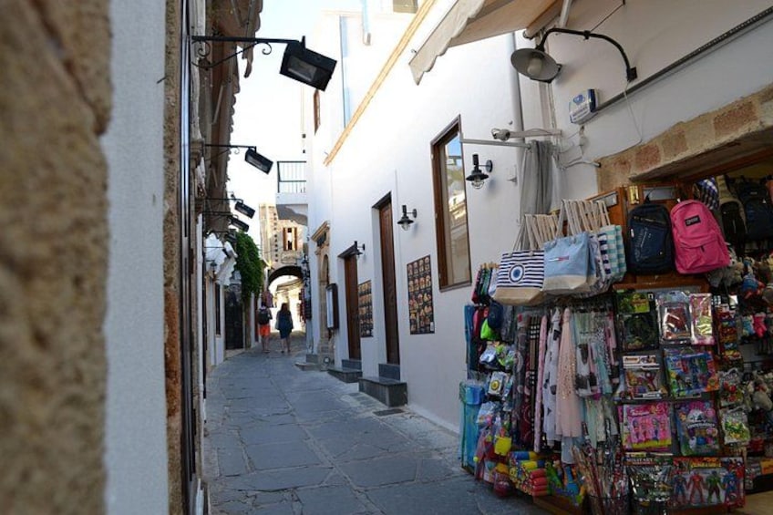 Una calle estrecha flanqueada por tiendas, incluyendo una con bolsas y juguetes de colores. 1