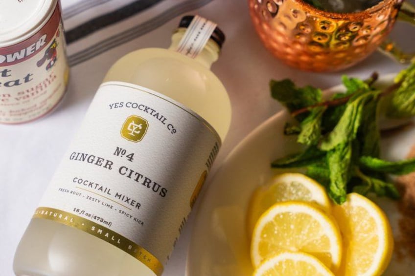 En flaska Yes Cocktail Co. No. 4, en blandning för drinkar med ingefära och citrus, ett glas vatten och en skål med citronskivor och myntablad. 2