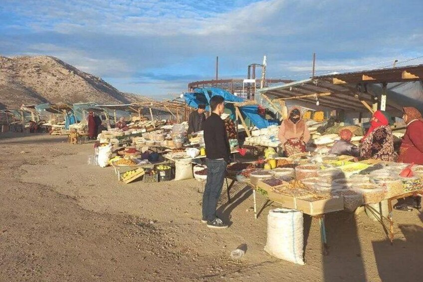 A market with people buying and selling goods, tents, and a mountainous background. 5