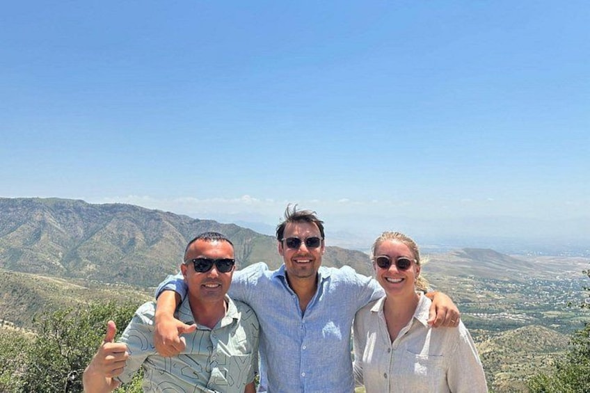 Three people standing on a hill with a mountainous landscape in the background. 2