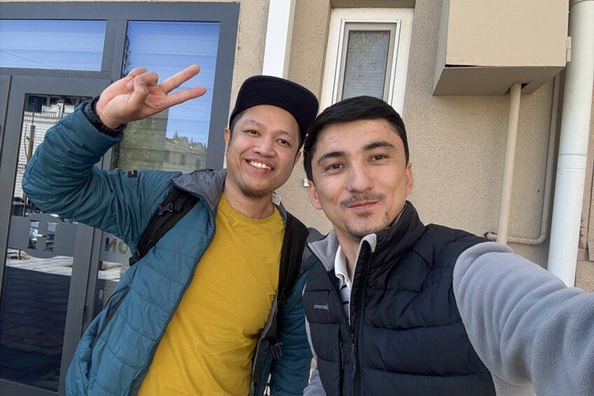 Two people taking a selfie with a building and a window in the background. 2