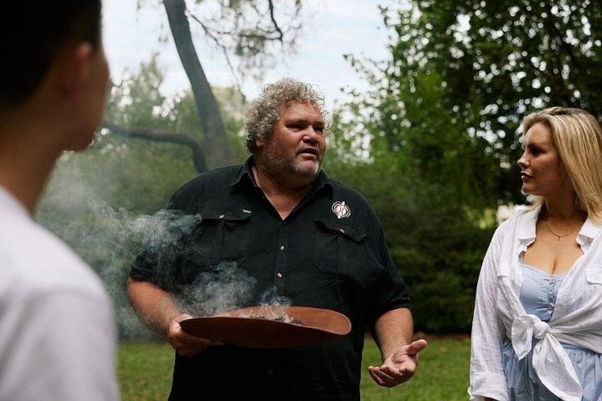 A person holding a bowl with smoke rising from it, standing outdoors with trees in the background. 1
