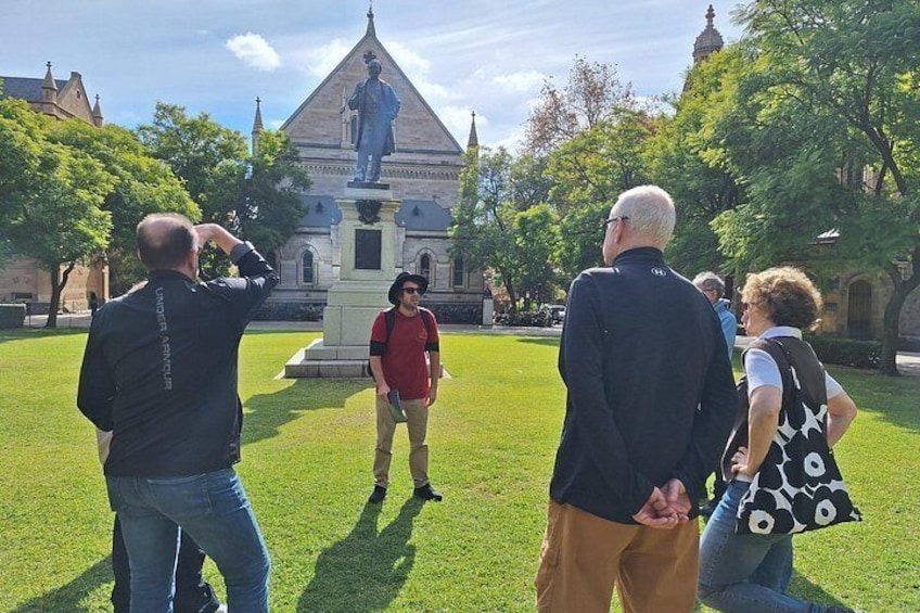 Un grupo de personas de pie en un área con césped, con una estatua y un edificio al fondo. 3