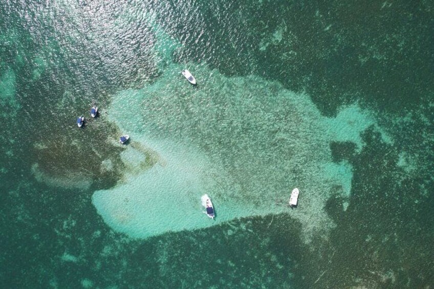 Vista aérea de un mar turquesa con varios barcos anclados cerca de un arrecife de coral. 1