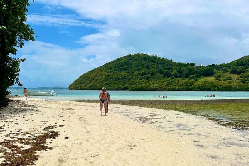 Una playa con gente caminando, un bote en el agua y una colina boscosa al fondo. 3