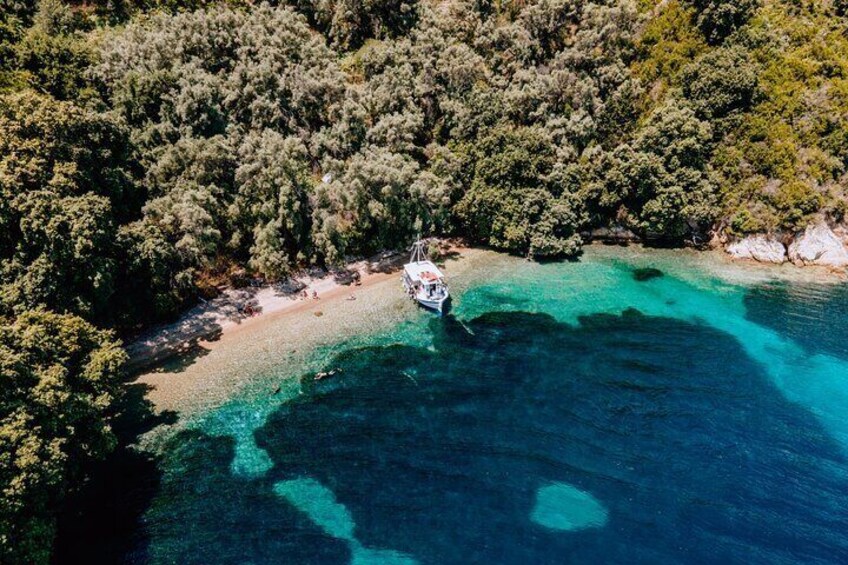 Oversigtsbillede af et kystområde med en båd på en turkis strand omgivet af tæt skov. 3