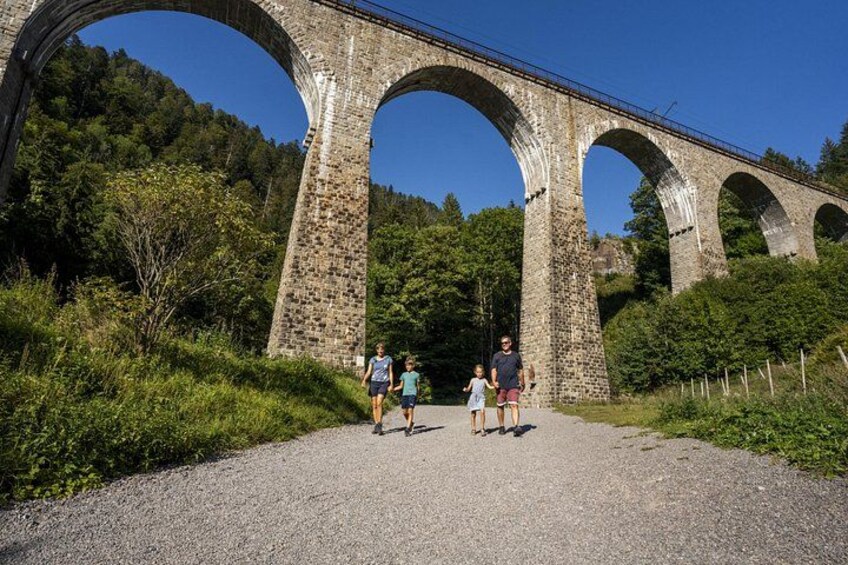 Un viaducto de piedra con múltiples arcos, rodeado de follaje y un sendero de grava. 2