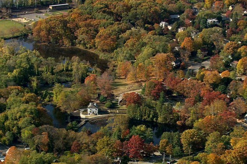 A river winding through a park with autumn foliage, a small white building, and a bridge. 2