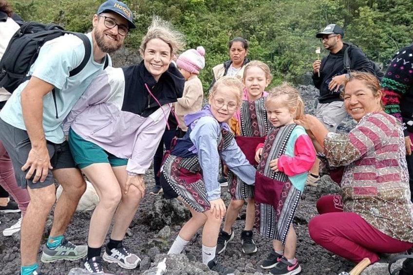 Un groupe de personnes, dont des enfants, s’est rassemblé sur un terrain rocheux, avec une végétation luxuriante en arrière-plan. 4