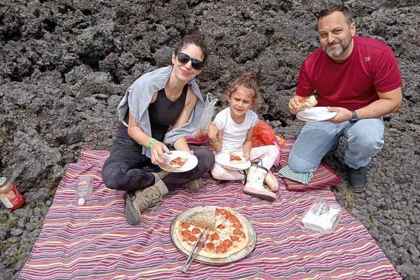 Une famille de trois personnes est assise sur une couverture à rayures, à l’extérieur, et partage une pizza. 5