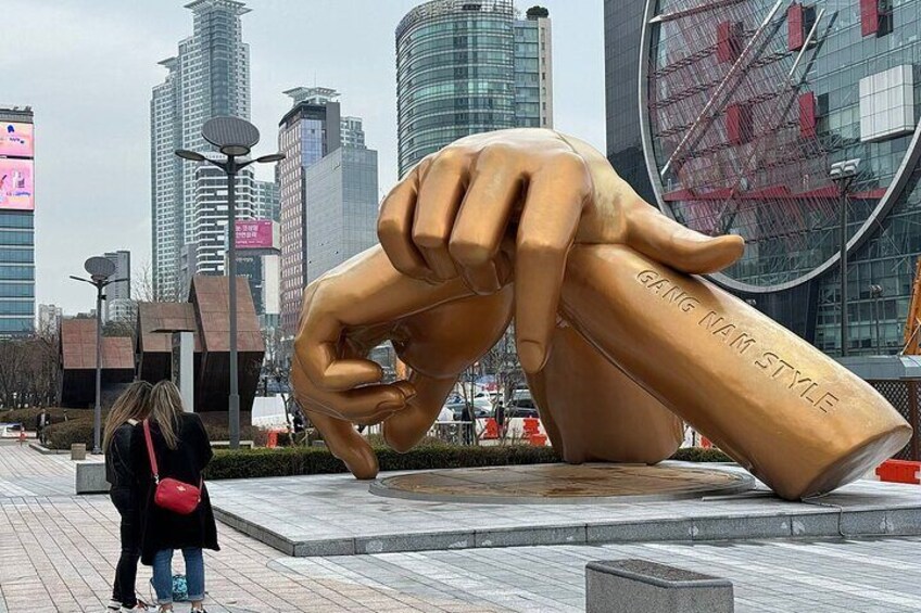 A large golden hand sculpture with the inscription "GANG NAM STYLE" in a city square with modern buildings in the background. 5