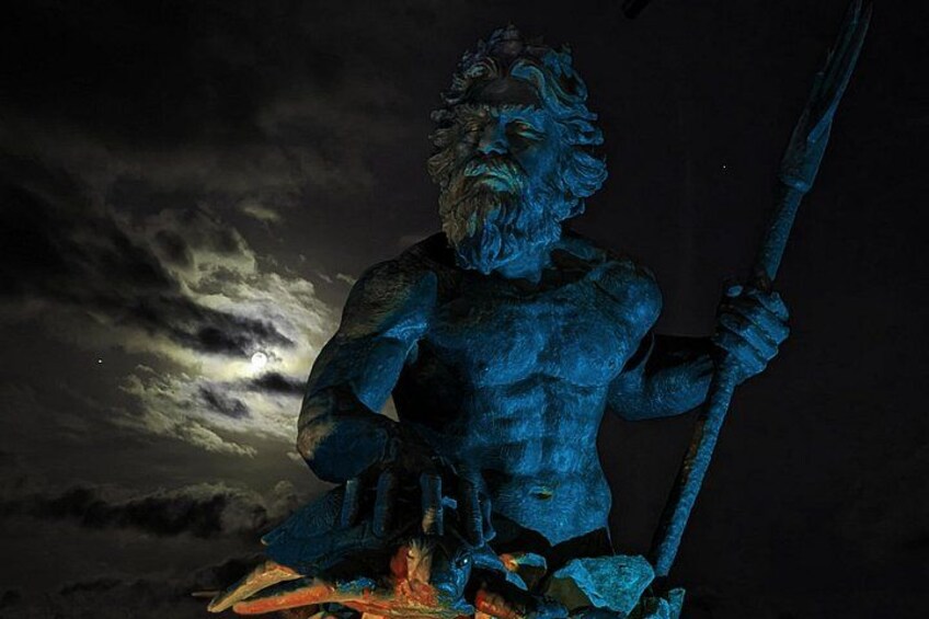 En statue af en skægget mand, der holder et trident, foran en nattehimmel med skyer. 2