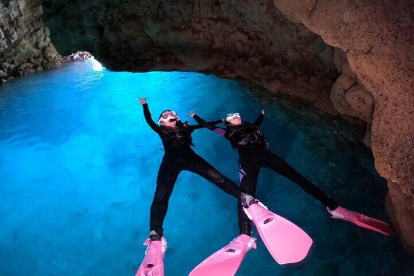 Two people scuba diving in a clear blue pool with rocky walls. 1