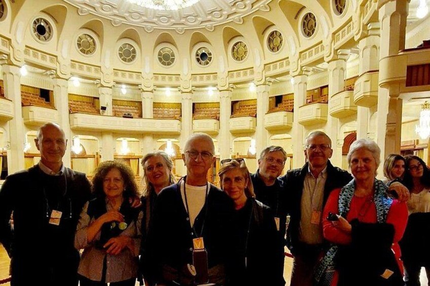Eine Gruppe von Menschen vor einem prächtigen, verzierten Gebäude mit mehreren Etagen und Balkonen. 4