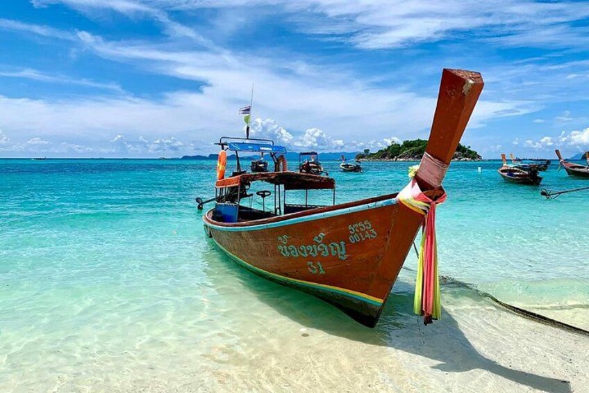 A wooden boat with a flag, anchored near a beach with clear turquoise water and other boats in the background. 4