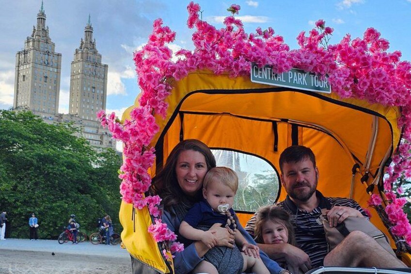 A family in a tent with a Central Park Tour sign, with a building in the background. 4