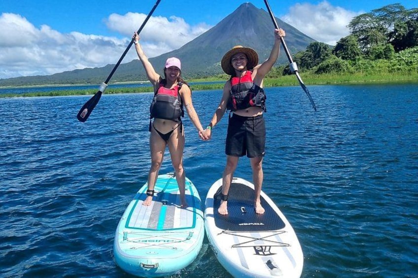 To personer står på paddleboards på en rolig sø med et bjerg i baggrunden. 2