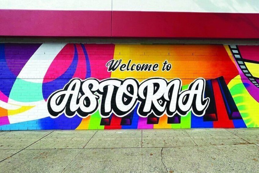 Ein farbenfrohes Wandgemälde mit dem Schriftzug 'Welcome to ASTORIA' an einem Gebäude. 1