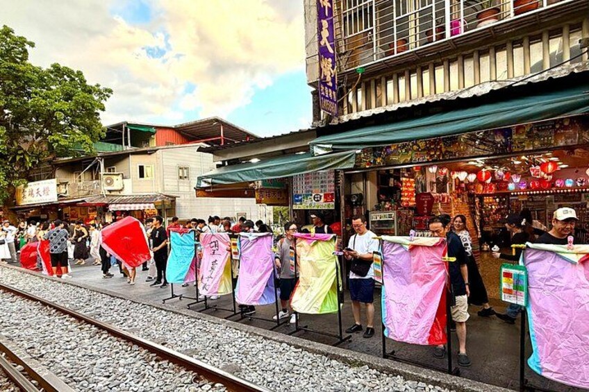 A street with colorful fabric barriers, a train track, and buildings with signs. 3