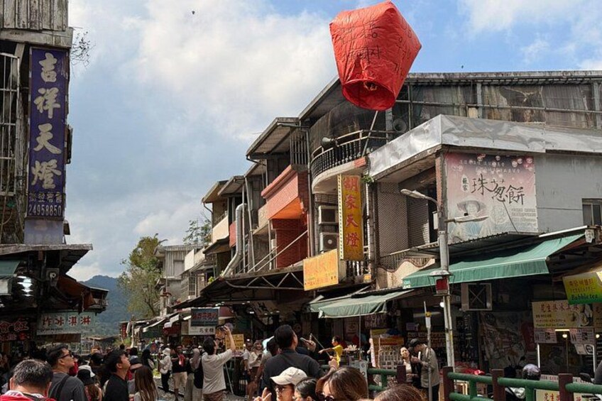 A crowded street with traditional buildings, a red lantern, and various signs. 2
