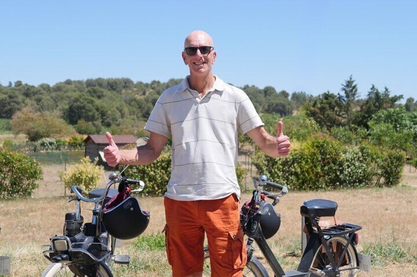 A person standing between two bicycles in an outdoor setting with trees and a clear sky in the background. 3