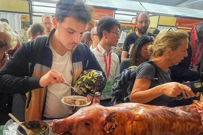 A man eating from a plate, a large roasted pig, and people in a crowded indoor setting. 2