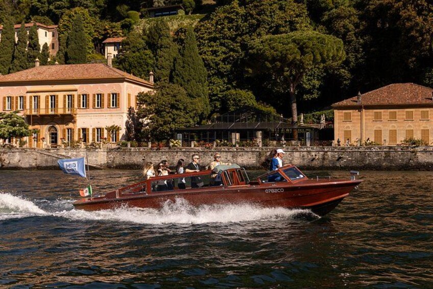 Un bateau à moteur rouge, transportant des passagers, se déplace sur une étendue d’eau, avec des bâtiments et des arbres en arrière-plan. 2
