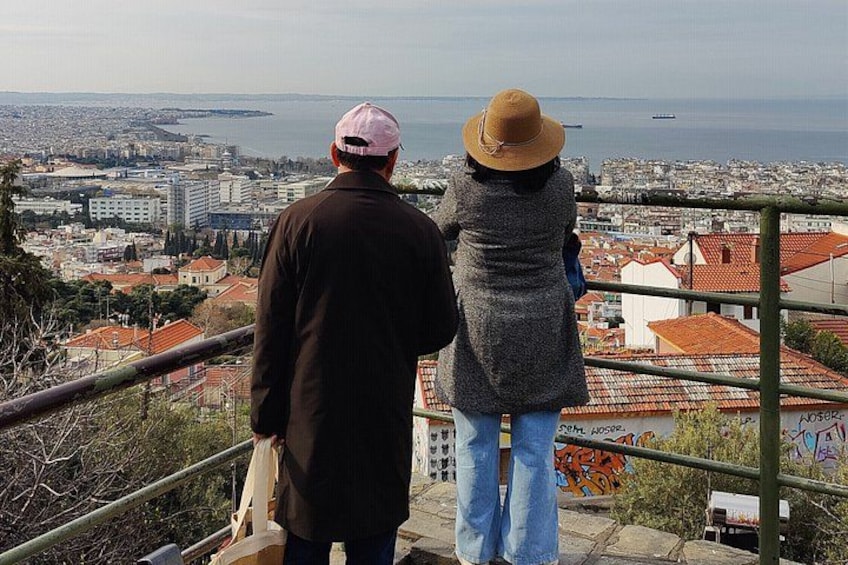 Two people overlooking a coastal cityscape with buildings and a sea view. 3