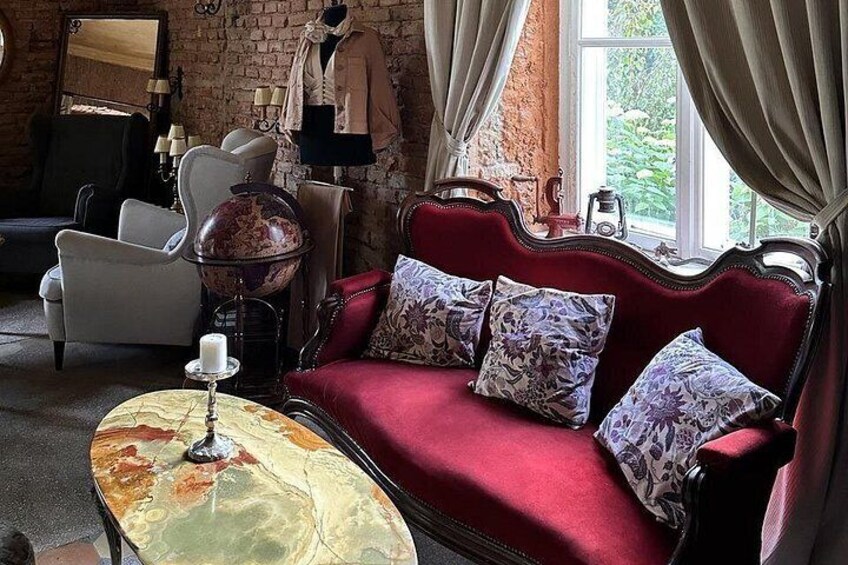 Ein rotes Sofa mit gemusterten Kissen, ein Globus und eine Lampe auf einem Tisch in einem Raum mit Backsteinwänden und einem Fenster. 2