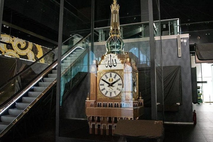 A large clock tower with Arabic calligraphy, a staircase, and modern architecture. 2