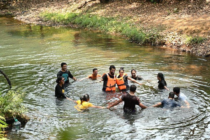 Un grupo de personas formando un círculo en un río poco profundo, rodeado de vegetación. 4
