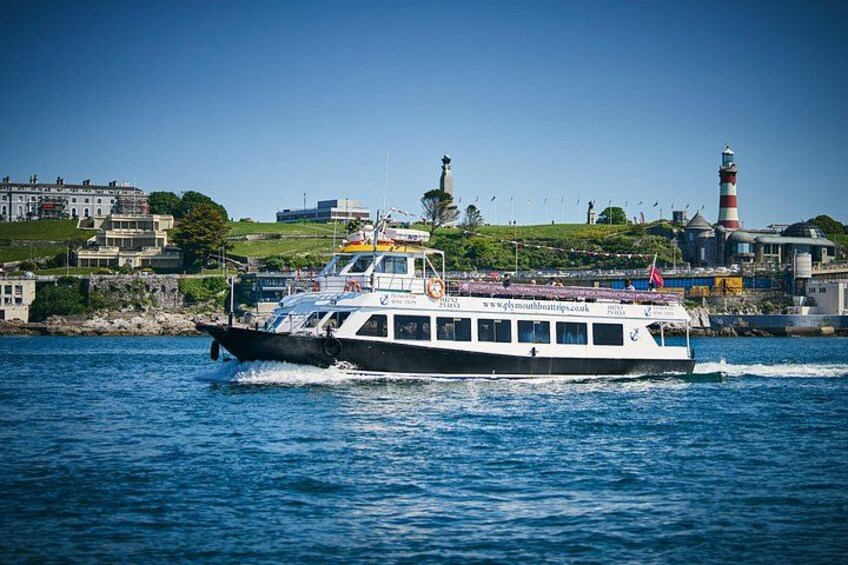 A ferry boat on a body of water with a lighthouse and buildings in the background. 2