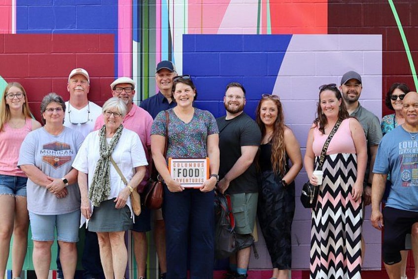 A group of people standing in front of a colorful wall with vertical stripes. 1