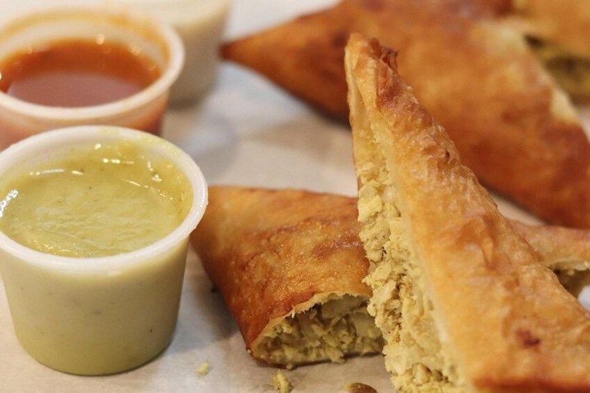 Un alimento, posiblemente una pastelería, con una capa dorada y un relleno que parece ser una mezcla de ingredientes. Hay dos recipientes pequeños con salsas, uno de color verdoso y el otro rojizo. 3