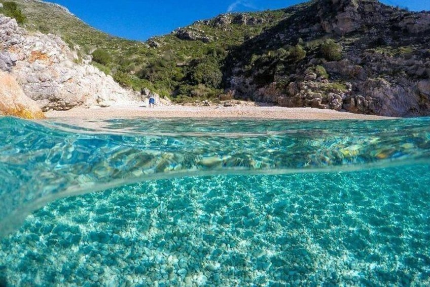Mar turquesa y cristalina con costa rocosa y una persona a lo lejos. 2