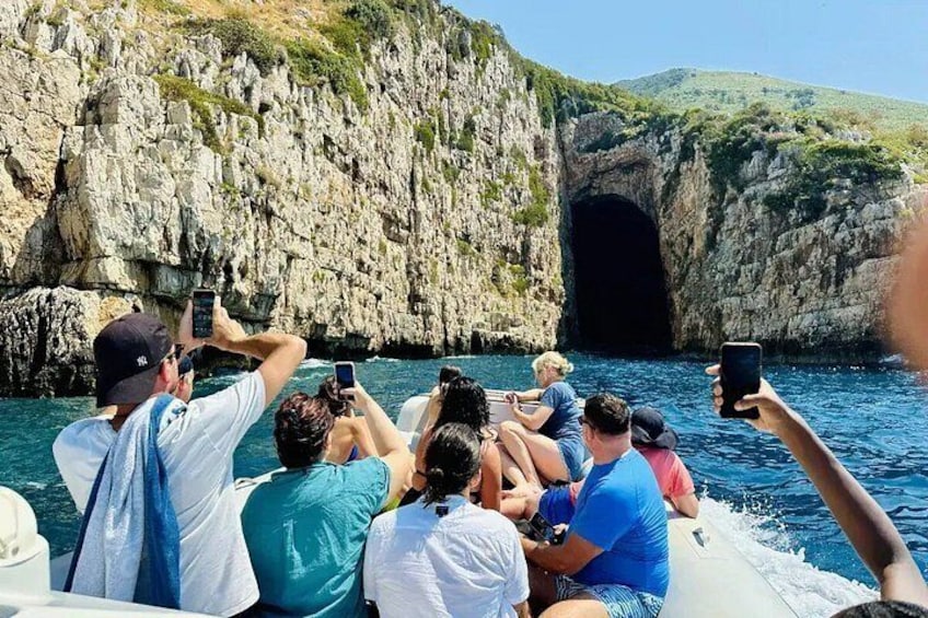 Un grupo de personas en un bote cerca de una costa rocosa con la entrada de una cueva. 1