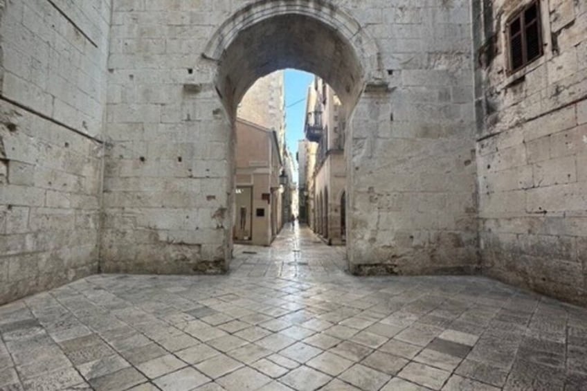 Une rue étroite, pavée de pierres, bordée de vieux bâtiments et menant à un portail en arc de cercle. 5