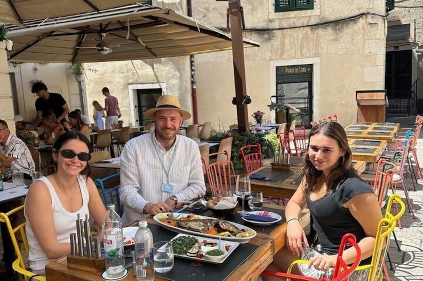 Un groupe de personnes est assis à une table dans un restaurant en plein air, où se trouvent également des chaises. 1