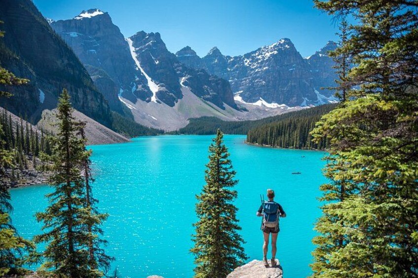 A person standing on a rock overlooking a turquoise lake surrounded by mountains. 1